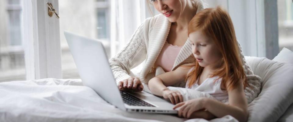 Mother and daughter using a laptop together in bed.