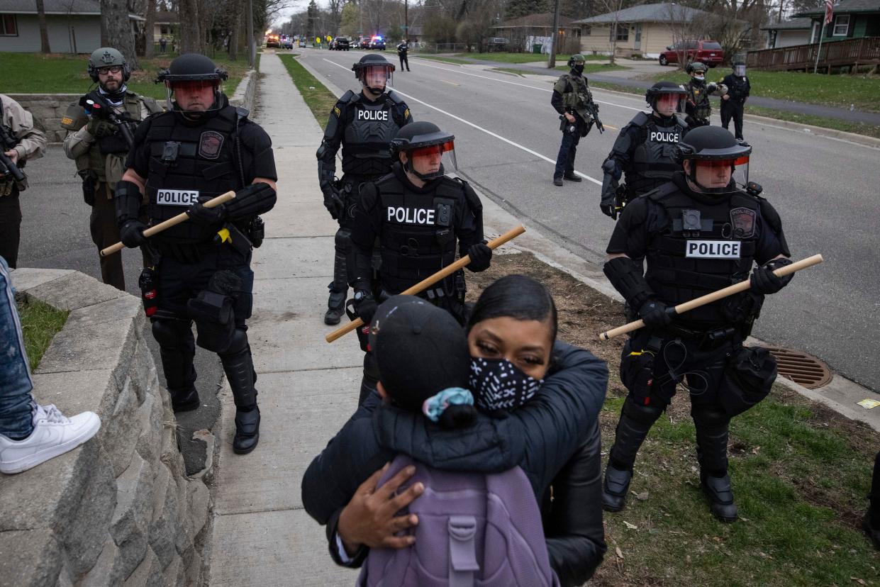 People hug as police officers stand armed behind them near the site of a shooting involving a police officer, Sunday, April 11, 2021, in Brooklyn Center, Minn.