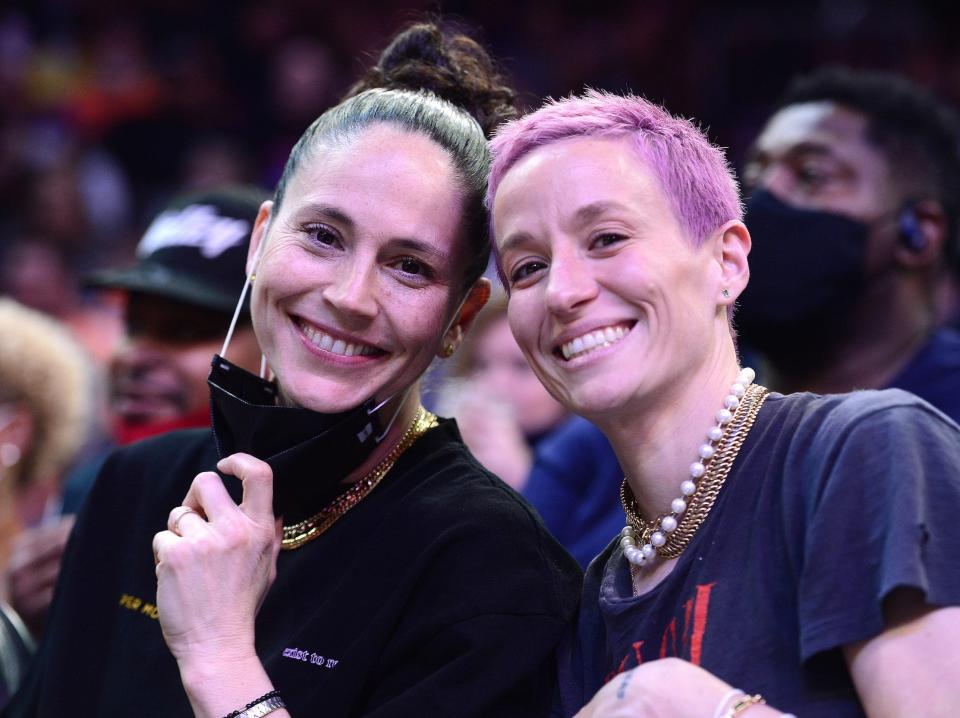 Sue Bird (left) and Megan Rapinoe pose from the sidelines of an NBA game.