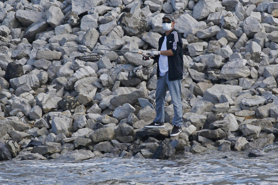 A fisherman observes social distancing while wearing a face mask as he prepares to cast his line Wednesday afternoon, March 25, 2020, at the Ross Barnett Reservoir spillway, near Brandon, Miss. Residents are taking advantage of warm weather in the outdoors and maintain social distancing as they fish. (AP Photo/Rogelio V. Solis)