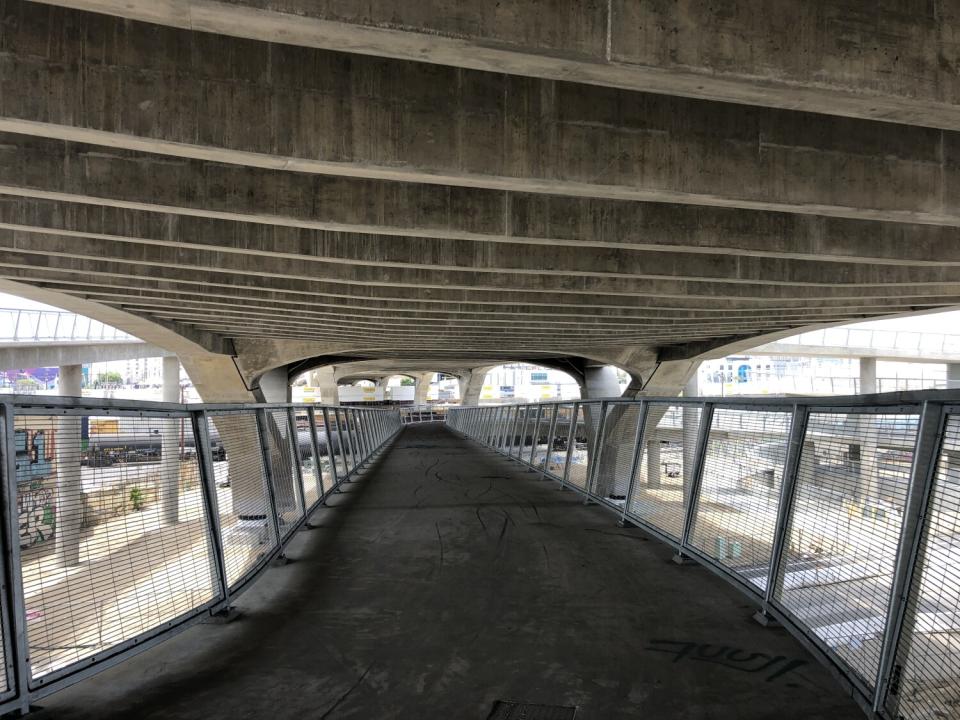 The ribbed concrete underside of the 6th Street Bridge is visible from a gently sloping ramp underneath the deck