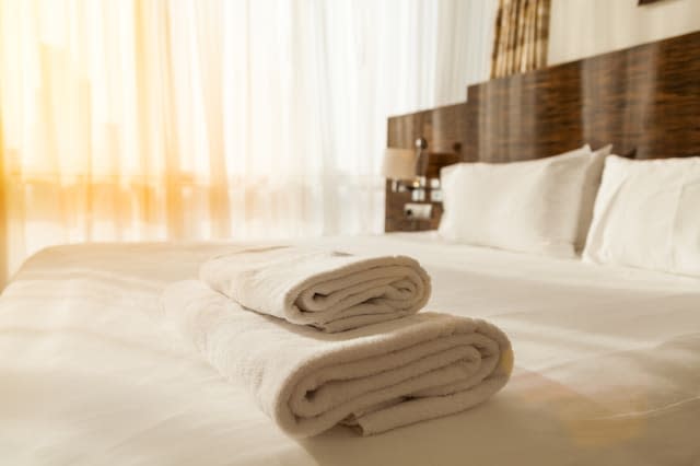 Stacked fresh white bath towels on the bed sheet. Close-up. Lens flair in sunlight