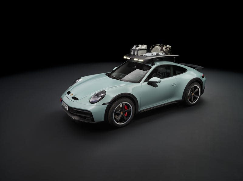 A grey-green 2023 Porsche 911 Dakar with roof rack parked in front of a black background.