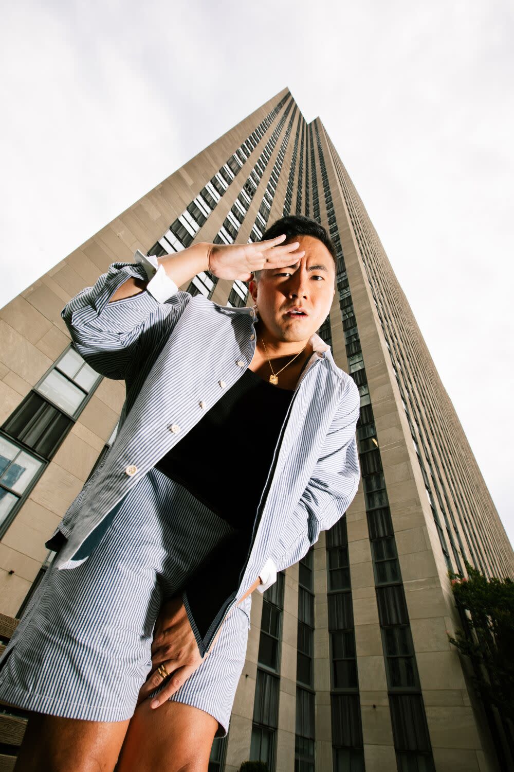 A man looks down with a hand to his face as he stands in front of a tall building