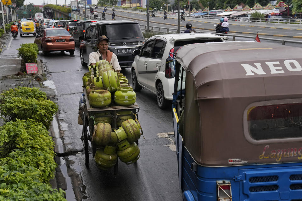 A worker transporting gas canisters pushes his cart against the traffic flow in Jakarta, Indonesia, Tuesday, Jan. 25, 2022. Indonesian parliament last week passed the state capital bill into law, giving green light to President Joko Widodo to start a $34 billion construction project this year to move the country's capital from the traffic-clogged, polluted and rapidly sinking Jakarta on the main island of Java to jungle-clad Borneo island amid public skepticism. (AP Photo/Dita Alangkara)