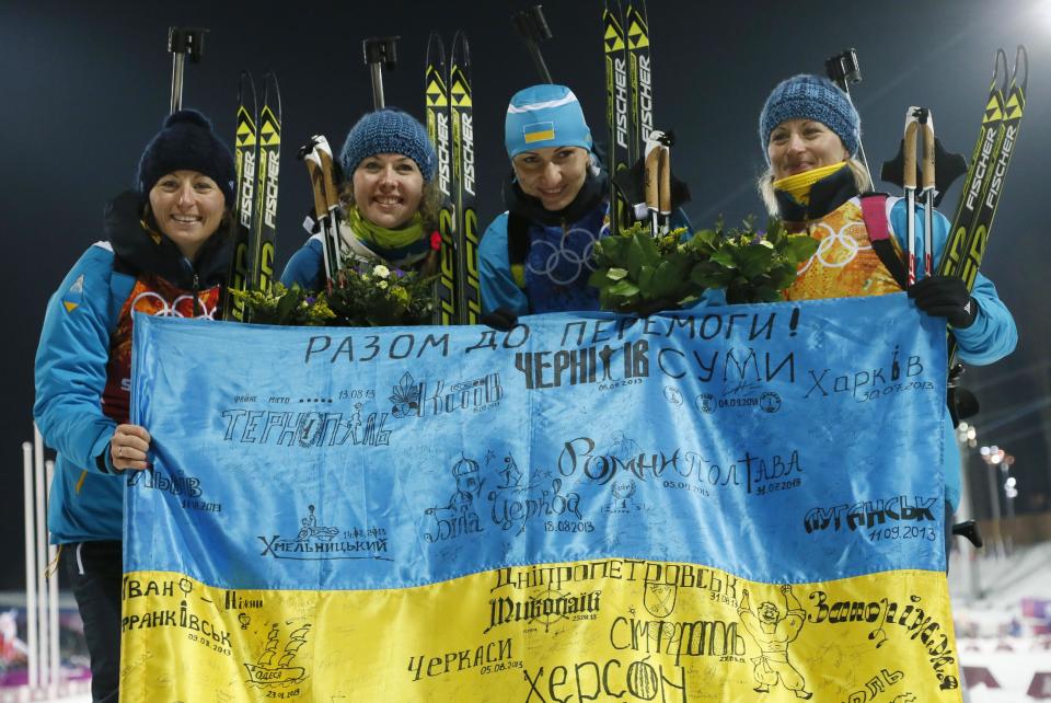 FILE - In this Friday, Feb. 21, 2014, file photo Ukraine's relay team Vita Semerenko, Juliya Dzhyma, Olena Pidhrushna and Valj Semerenko, from left, celebrate with a Ukrainian flag with writings on it after winning the gold during the women's biathlon 4x6k relay, at the 2014 Winter Olympics in Krasnaya Polyana, Russia. With the crisis in Ukraine escalating by the day, the prospect of holding the Winter Olympics in the former Soviet republic seems hard to imagine. Yet, the western Ukrainian city of Lviv hasn’t given up on its bid for the 2022 Games. Lviv remains among the five contenders in what is turning into a very unstable race, vying with Almaty, Kazakhstan; Beijing; Krakow, Poland; and Oslo. (AP Photo/Dmitry Lovetsky, File)