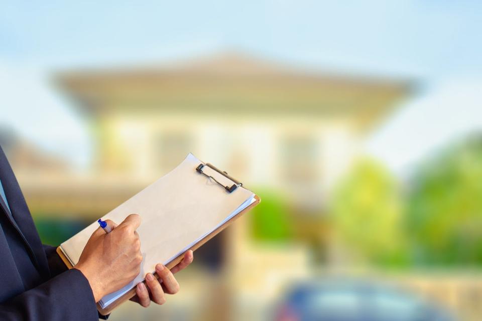 clipboard for home inspection in front of blurry house