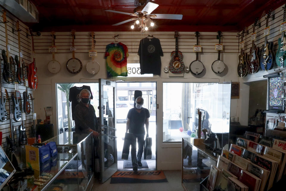 A customer is silhouetted as he carries three guitars for repairs at Pittsburgh Guitars as it opened its doors to walk-in customers for the first time since March as counties in southwestern Pennsylvania join northwestern and the north central regions with more relaxed COVID-19 prevention restrictions, Friday, May 15, 2020, in Pittsburgh. (AP Photo/Keith Srakocic)