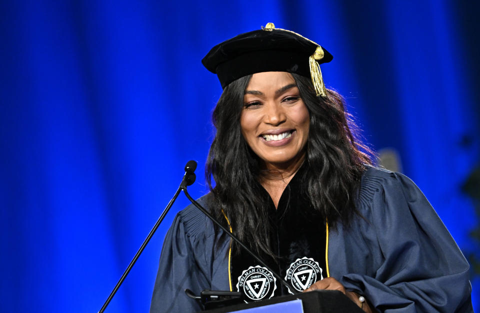 Angela Bassett smiles while wearing academic regalia and speaking at a podium during a graduation ceremony