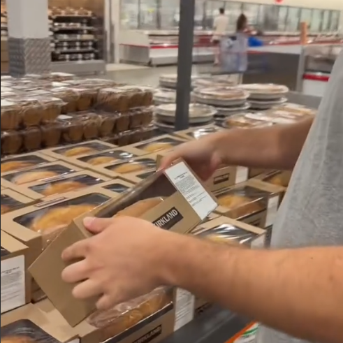 Person placing a Costco bakery item on shelf in a grocery store's bakery section