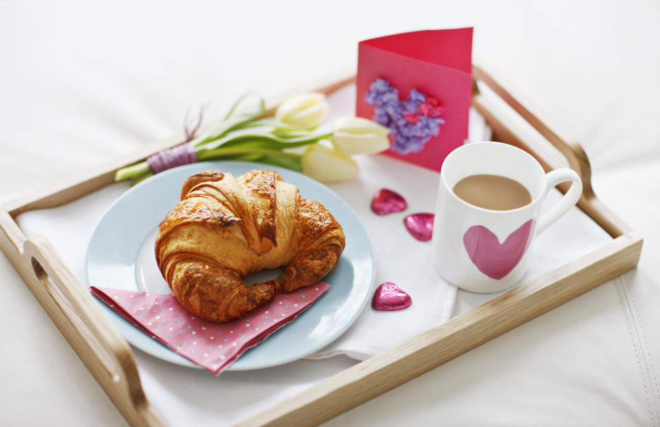 Frühstückstablett mit Croissant auf dem Teller, Kaffee in einer Herztasse, Schokoladenherzen, Blumen und einer Karte