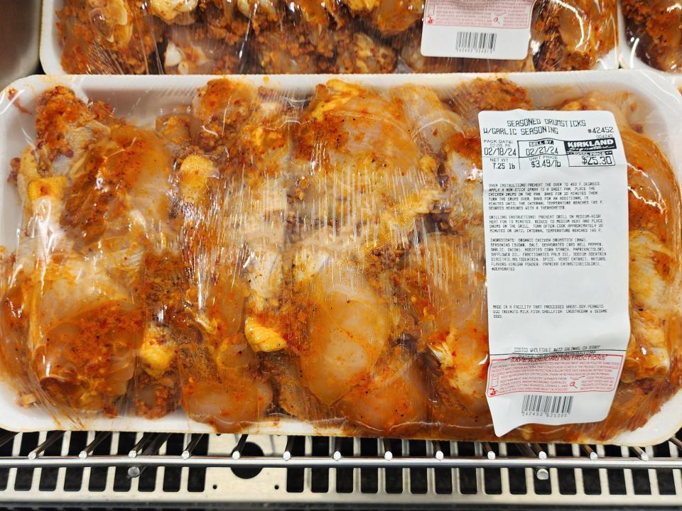 A package of raw drumsticks with a red-orange garlic seasoning  on a white tray with a Kirkland Signature label