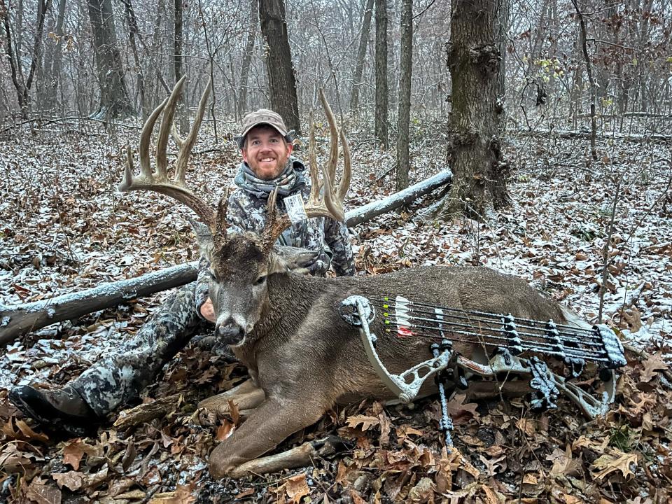 A bowhunter grins while sitting behind a big Iowa buck.