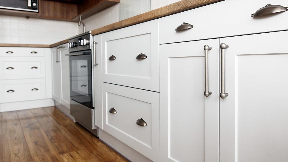 Stylish light gray handles on cabinets close-up, kitchen interior with modern furniture and stainless steel appliances.