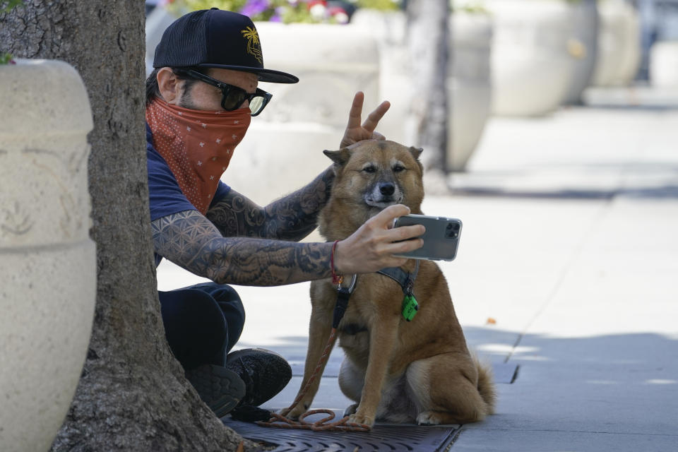 Andrew Stuart wears a bandana as a mask while taking a selfie with his dog, Voltron, on Sunset Blvd, Thursday, July 2, 2020, in West Hollywood, Calif. Sheriff's deputies in West Hollywood will issue citations to people who are not wearing masks in public, ramping up enforcement that previously had largely been imposed without penalties. (AP Photo/Ashley Landis)