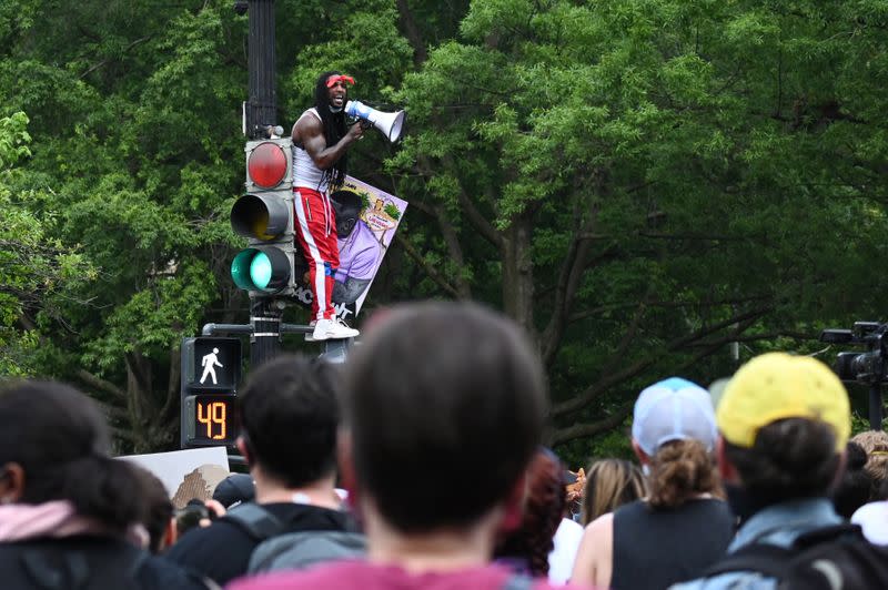 A man on top of a traffic signal leads a crowd in chants during a protest against the death in police custody of George Floyd