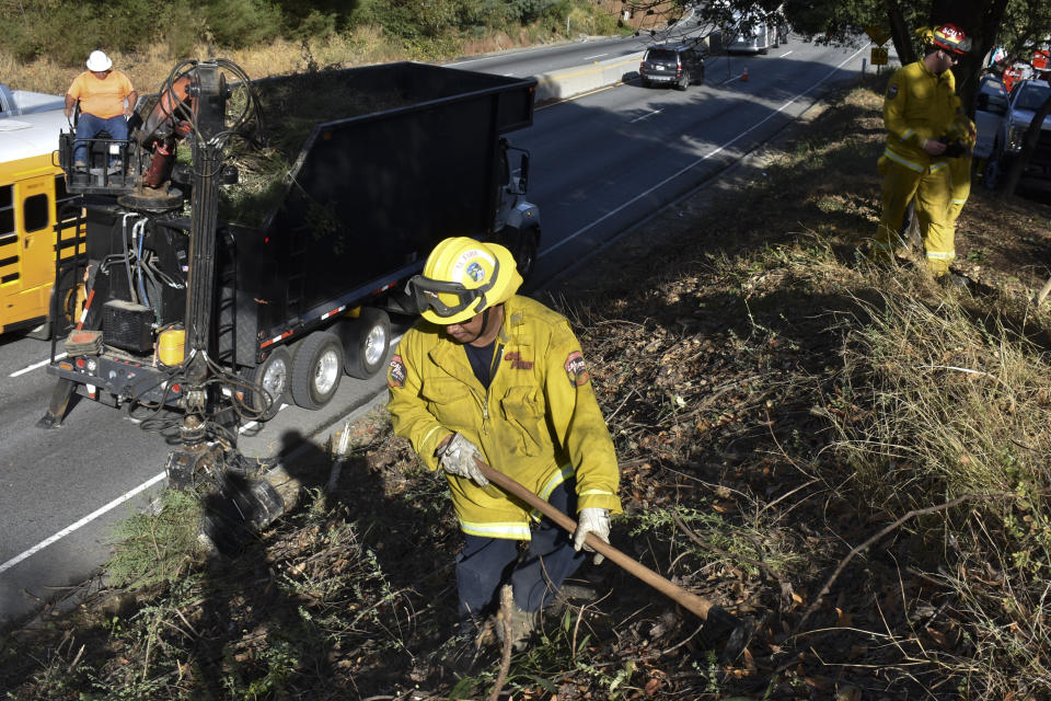 A fire prevention crew removes vegetation along California's Route 17 on Wednesday, Nov. 20, 2019, near Redwood Estates, Calif. Authorities are rushing to clear vegetation in high-risk communities after fires killed 149 people and destroyed almost 25,000 homes in the state over the past three years. (AP Photo/Matthew Brown)