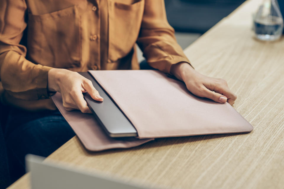 Unrecognisable woman in a yellow shirt taking her laptop pc out of the bag at work. (Getty Images)