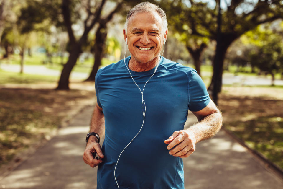 Portrait of a senior man in fitness wear running in a park. Close up of a smiling man running while listening to music using earphones.