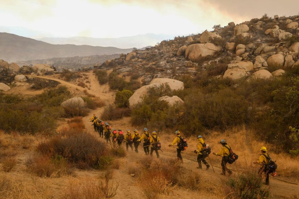 Firefighters walk in a line to battle the Fairview Fire burning on a hillside on Sept. 8 near Hemet, Calif.