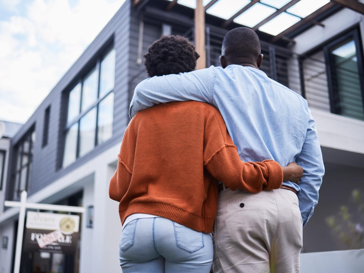 Rearview shot of a young couple standing outside their new home.