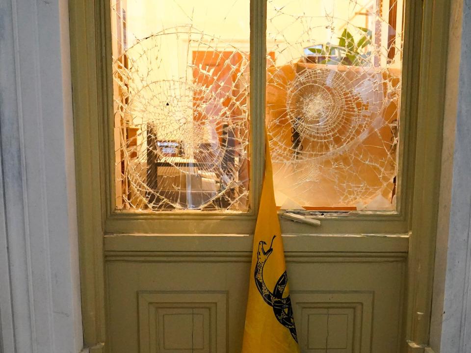 A flag hangs between broken windows after then-President Donald Trump supporters tried to break through police barriers outside the US Capitol