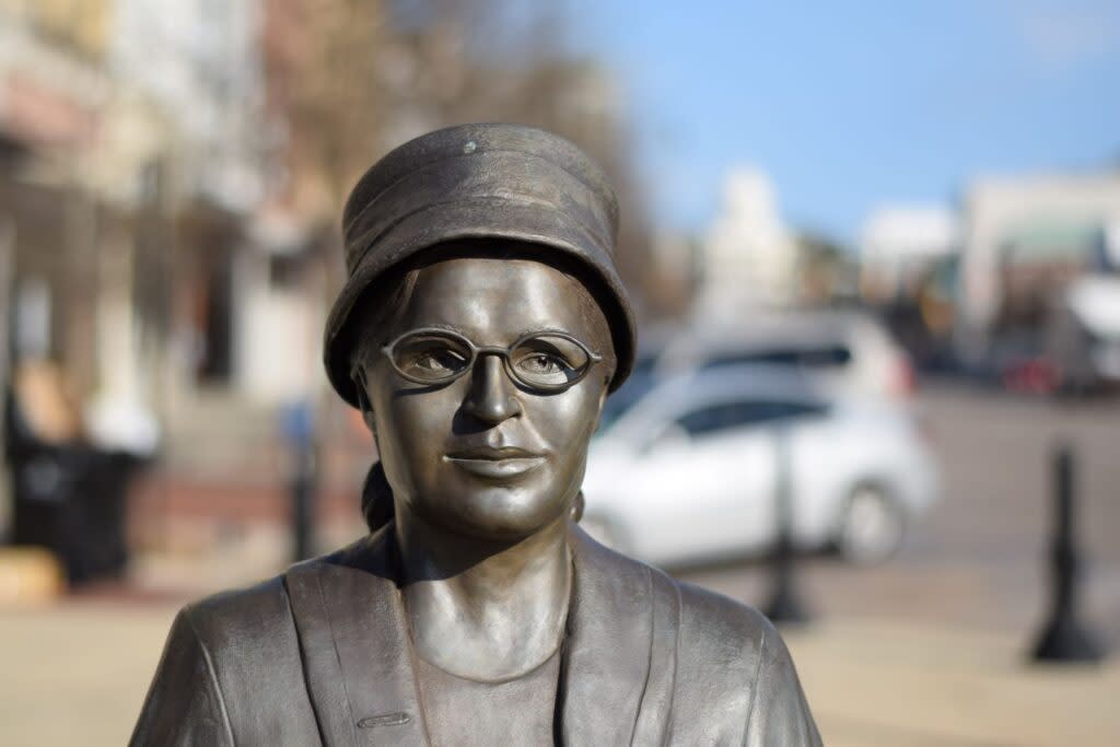 A bronze statue of Rosa Parks shows her wearing a pillbox hat, oval glasses and a winter coat.