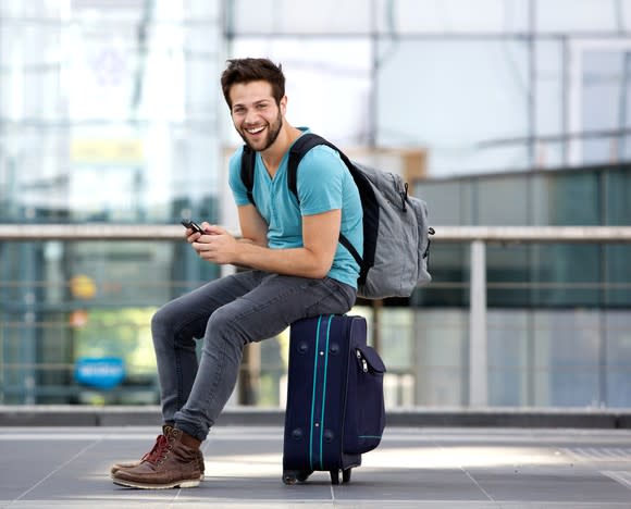 Man sitting on suitcase wearing backpack