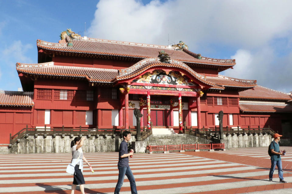 In this October 2016, photo, people walk in front of the main temple of Shuri Castle in Naha, Okinawa, southern Japan. A fire spread among structures at Shuri Castle on Thursday, Oct. 31, 2019, on Japan's southern island of Okinawa, nearly destroying the UNESCO World Heritage site. (Kyodo News via AP)