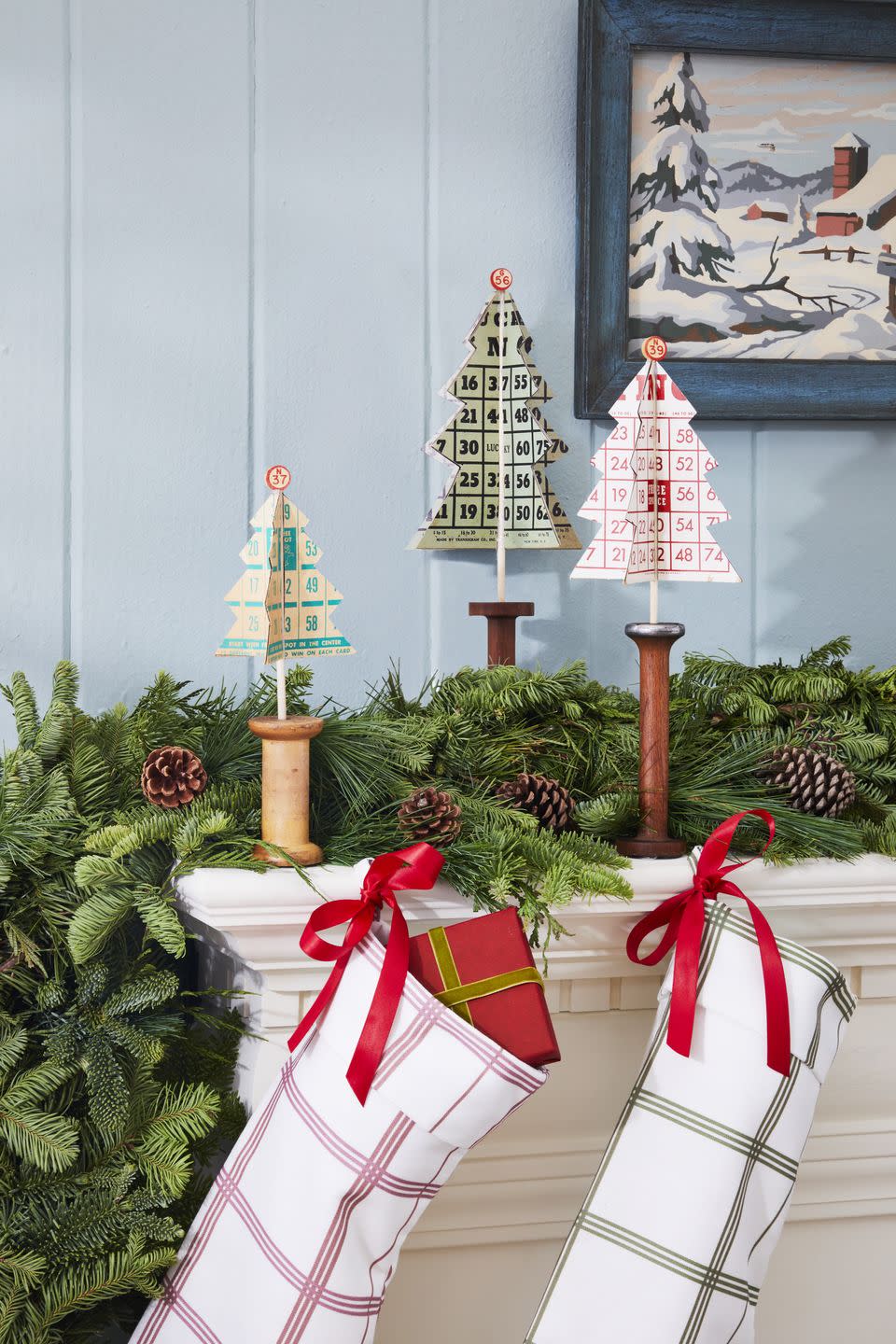 christmas trees made from vintage bingo cards set in antique wooden spools all displayed on a decorated mantel