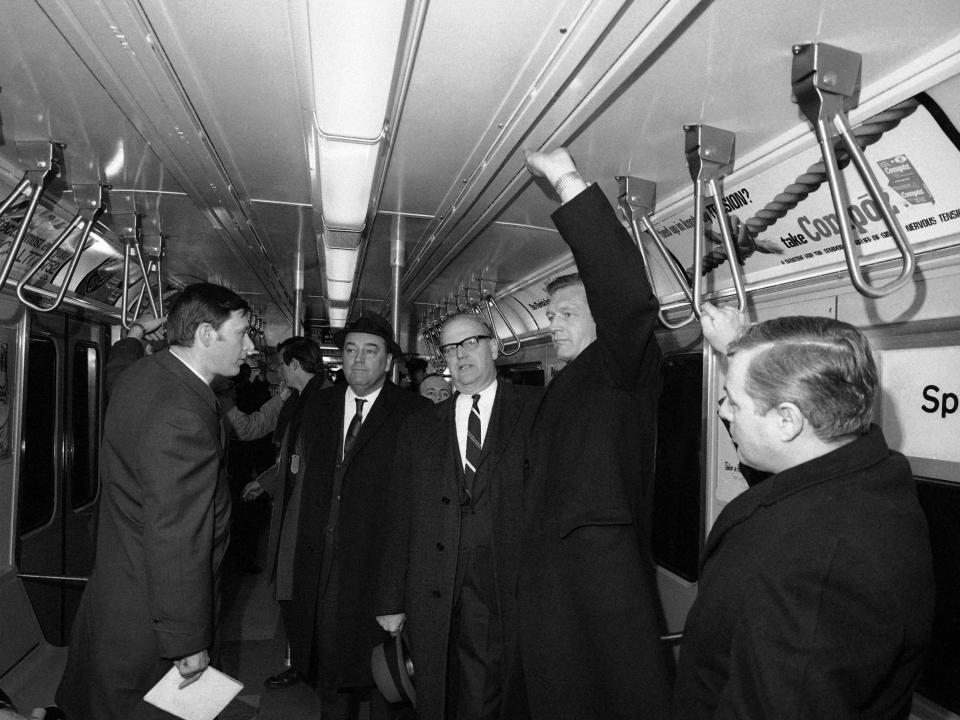 New York Mayor John V. Lindsay, right, accompanied by William Ronan, center, and newsmen stand inside a subway car.