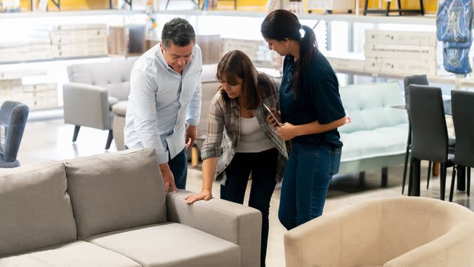 Happy couple buying a couch at a home improvement store and talking to a saleswoman - business concepts.