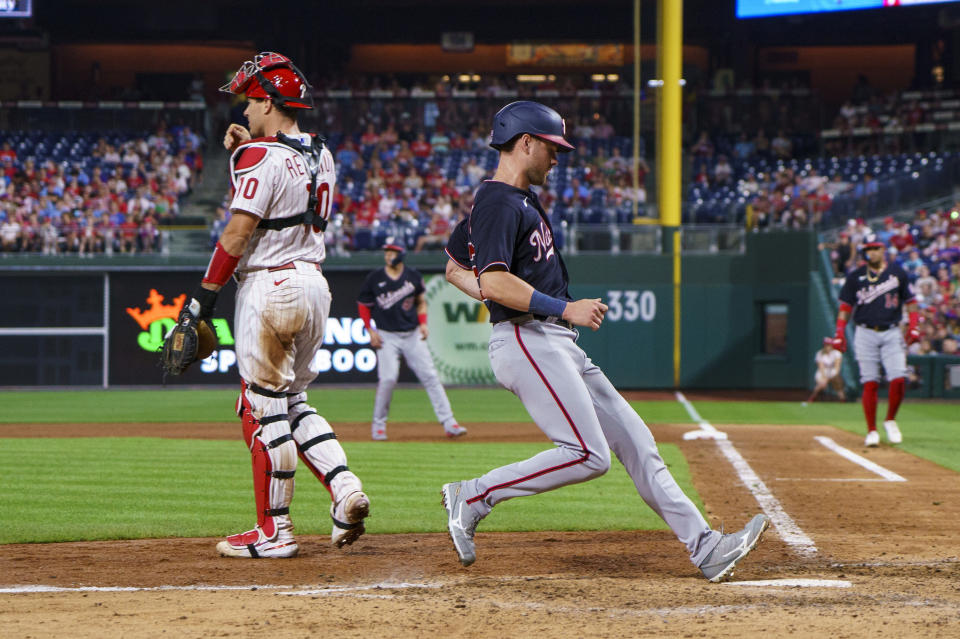 Washington Nationals' Lane Thomas, right, comes in to score on a sacrifice fly by Ildemaro Vargas as Philadelphia Phillies catcher J.T. Realmuto, left, looks on during the eighth inning of a baseball game, Friday, Aug. 5, 2022, in Philadelphia. (AP Photo/Chris Szagola)