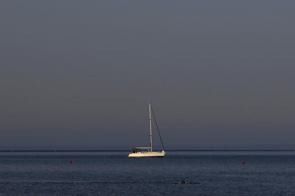 A swimmer passes in front of a yacht at Makenzi beach in the southern coastal city of Larnaca, Cyprus, Monday, May 30, 2022. Hundreds of Russian and Ukrainian Orthodox faithful visiting Cyprus would stream daily past the icon of the Virgin Mary at Kykkos Monastery to venerate the relic that tradition dictates was fashioned by Luke the Evangelist and blessed by the Virgin herself. But a European Union ban on flights to and from Russia as a result of Russia's invasion of Ukraine has meant a loss of 800,000 vacationers - a fifth of all tourists to Cyprus in record-setting 2019. (AP Photo/Petros Karadjias)