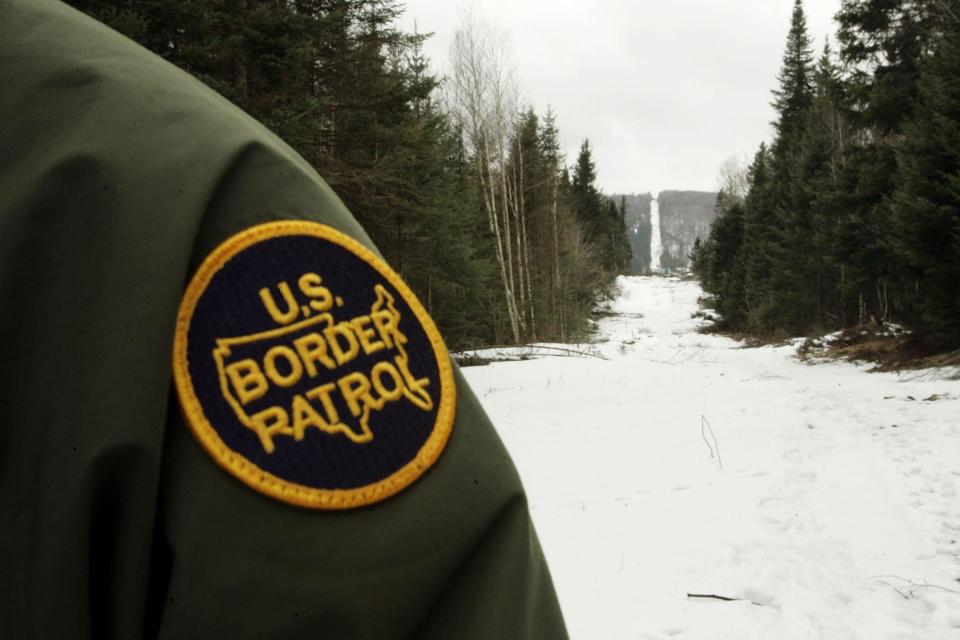 A Border Patrol agent works along the boundary marker cut into the forest between Canadian territory on the right and Vermont on the left.