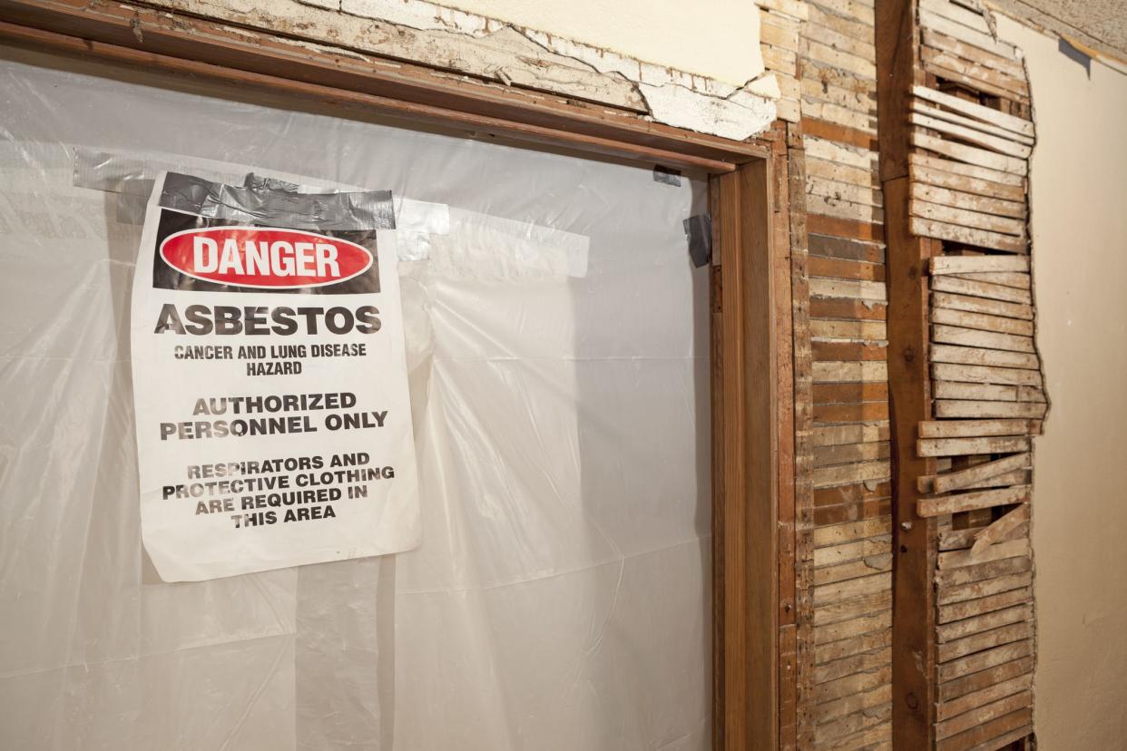 A danger asbestos warning sign taped, hanging on a sealed off doorway inside an older house.