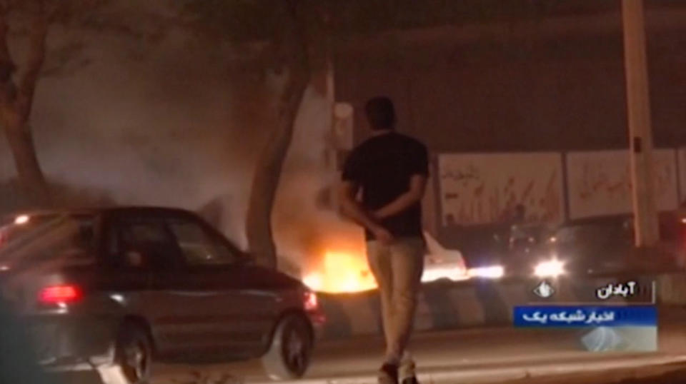 In this Saturday, Nov. 16, 2019 image from video aired by Iran's Islamic Republic of Iran Broadcasting state television channel, a man walks past a fire set by protesters in Abadan, Iran. Protesters angered by Iran raising government-set gasoline prices by 50% blocked traffic in major cities and occasionally clashed with police Saturday after a night of demonstrations punctuated by gunfire, violence that reportedly killed at least one person. (IRIB via AP)