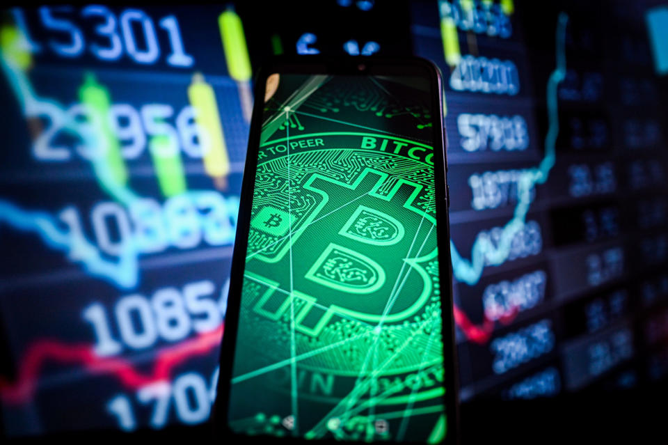 Ein Bitcoin-Logo auf einem Smartphone, im Hintergrund die Börsenkurse. - Copyright: Omar Marques/SOPA Images/LightRocket via Getty Images