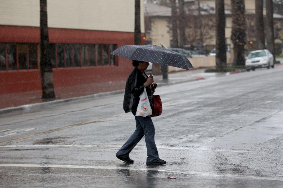 A pedestrian uses an umbrella while walking across the street in downtown Riverside as the second major El Niño storm of the season brings heavy rainfall, road closures and flooding to the southland on Jan. 6, 2016.