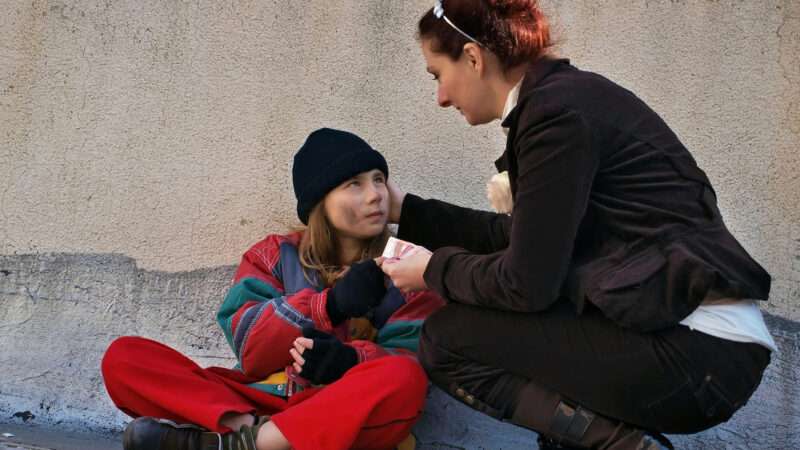 Woman giving food and clothing to another homeless woman