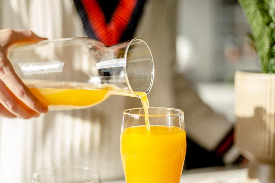 A person pours orange juice into a glass