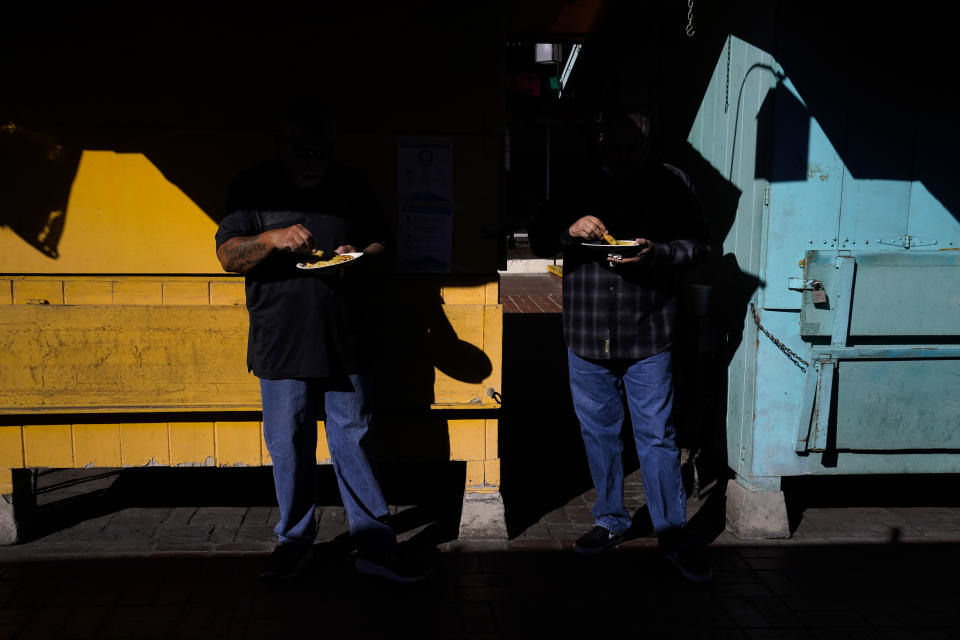 Two customers eat their lunch in front of shuttered market stalls on Olvera Street in downtown Los Angeles, Wednesday, Dec. 16, 2020. Olvera Street, known as the birthplace of Los Angeles, has been particularly hard hit by the coronavirus pandemic, with shops and restaurants closed and others barely hanging on. Only a handful of businesses remain open on weekdays as tourism has cratered and downtown offices are closed and festive events held throughout the year have been canceled. (AP Photo/Jae C. Hong)