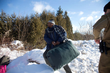 A man who claimed to be from Sudan throws his family's suitcases towards the border as he is detained by a U.S. border patrol officer after his family crossed the U.S.-Canada border into Hemmingford, Canada, from Champlain in New York, U.S., February 17, 2017. REUTERS/Christinne Muschi