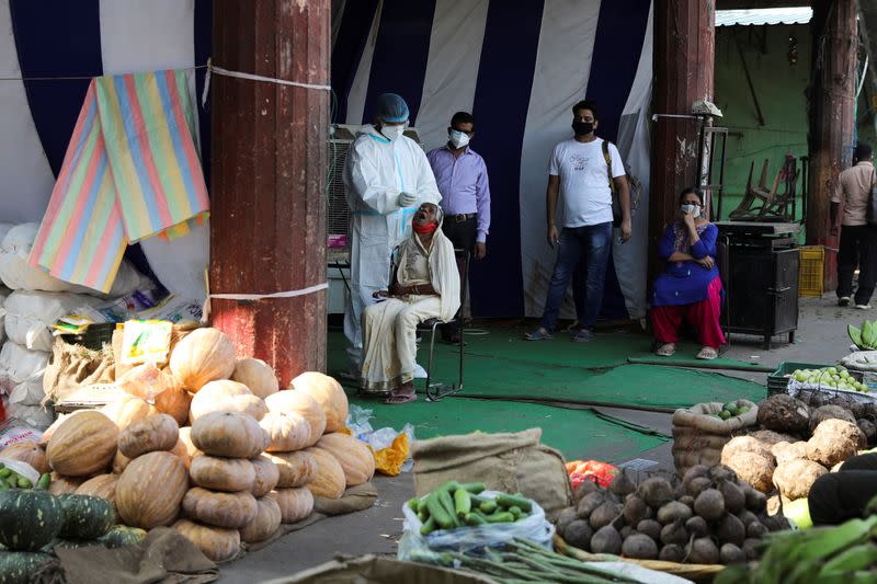Health worker collects a swab sample from a woman at a vegetable market, in New Delhi