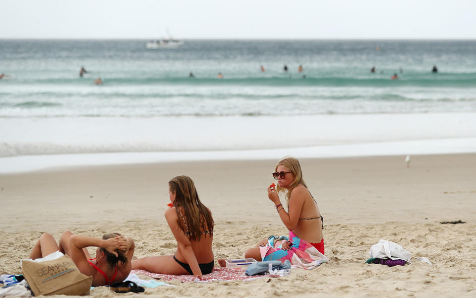 Three women in bikinis shows sitting on a beach on the Gold Coast.