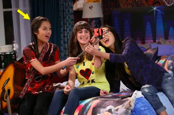 Olivia Rodrigo, Madison Hu, and another girl take a selfie while sitting on a bed. Olivia holds a guitar, and Madison is holding a selfie stick