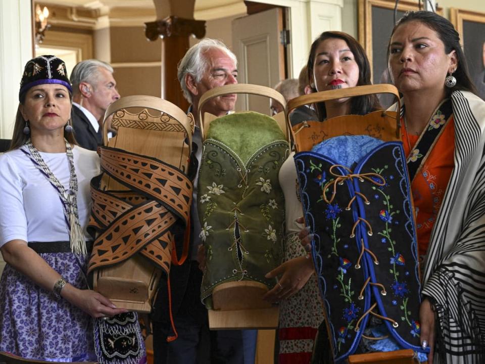 Michelle Schenandoah, Rosalie LaBillois and Jonel Beauvais hold cradleboards ahead of a gathering between Pope Francis and a delegation of Indigenous people at the archbishop's residence in Quebec City on July 29, 2022. Regional Chief of the Assembly of First Nations of Quebec and Labrador Ghislain Picard is seen in the background. (Ciro Fusco/The Associated Press - image credit)