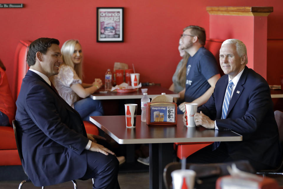 Vice President Mike Pence, right, talks to Florida Gov. Ron DeSantis as they wait for their lunch at Beth's Burger Bar, Wednesday, May 20, 2020, in Orlando, Fla. Pence is scheduled to participate in a roundtable discussion with hospitality and tourism industry leaders to discuss their plans for re-opening during the coronavirus outbreak. (AP Photo/Chris O'Meara)