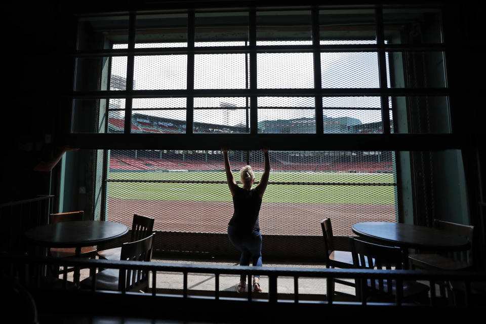 In this June 25, 2020, photo, general manager Maggie Flynn opens a large window with a view of Fenway Park from the Bleacher Bar in Boston. Located inside the outfield structure at Fenway, it might be one of the few places where fans can watch live MLB baseball this year. Like the Knothole Gangs of the sport's early days, fans hoping to catch a glimpse of a ballgame in person this season will be pressing their faces up against hotel windows, peering through metal grates or clambering up to rooftops when baseball returns this month in otherwise empty stadiums. (AP Photo/Elise Amendola)