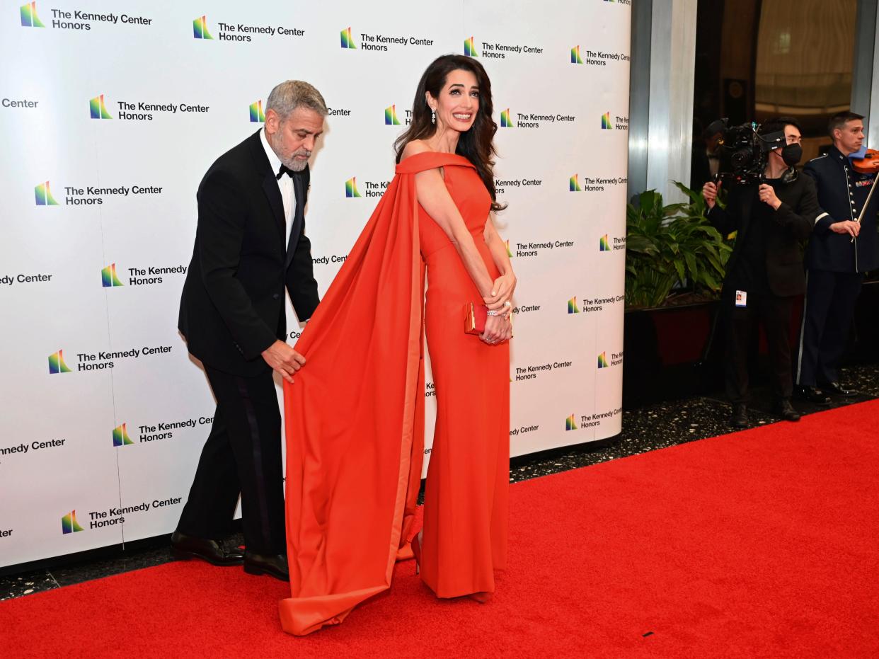 George Clooney fixing the dress of his wife, Amal Clooney, at the State Department for the Kennedy Center Honors gala dinner on December 3, 2022.